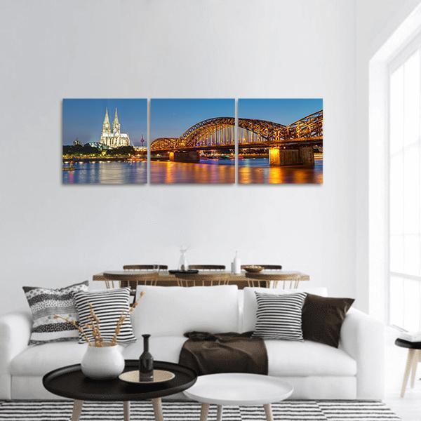 Hohenzollern Bridge with Cologne Cathedral Spires Panoramic Canvas Wall Art in orange, yellow and blue, hung on a wall