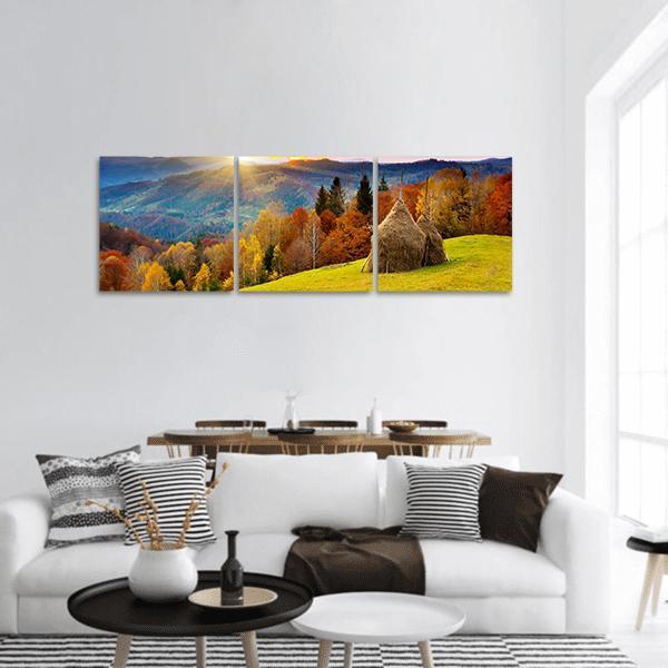 Autumn Mountain Landscape with Conical Haystacks Panoramic Canvas Wall Art in orange, yellow and blue, hung on a wall