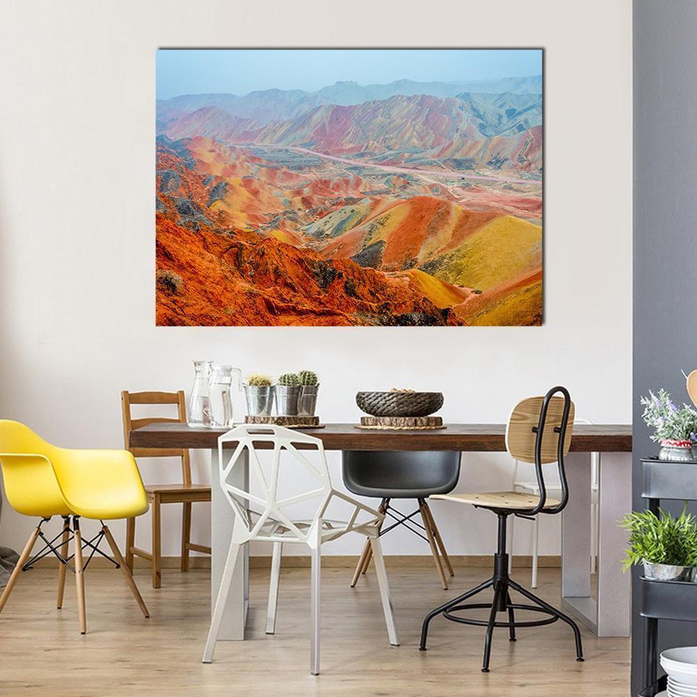 Vibrant Rainbow Mountain Landscape Canvas Wall Art in red, orange and multicolor, single panel hung on a wall