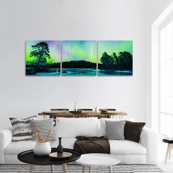 Colorful Northern Lights Over Pine Lake Panoramic Canvas Wall Art in green, blue and purple, single panel hung on a wall