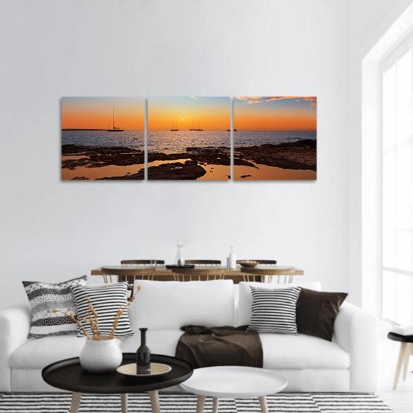 Ibiza Sunset with Silhouetted Sailboats Panoramic Canvas Wall Art in black, orange and blue, hung on a wall
