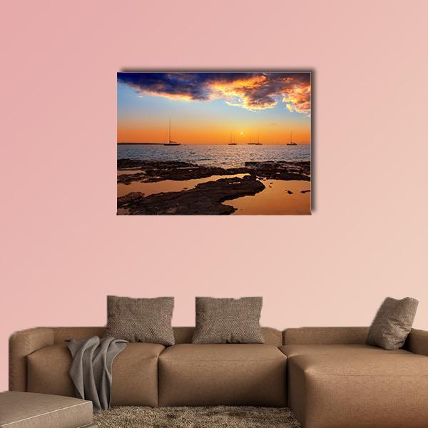 Sunset Over Rocky Shore with Sailboats Canvas Wall Art in orange, yellow and blue, single panel hung on a wall