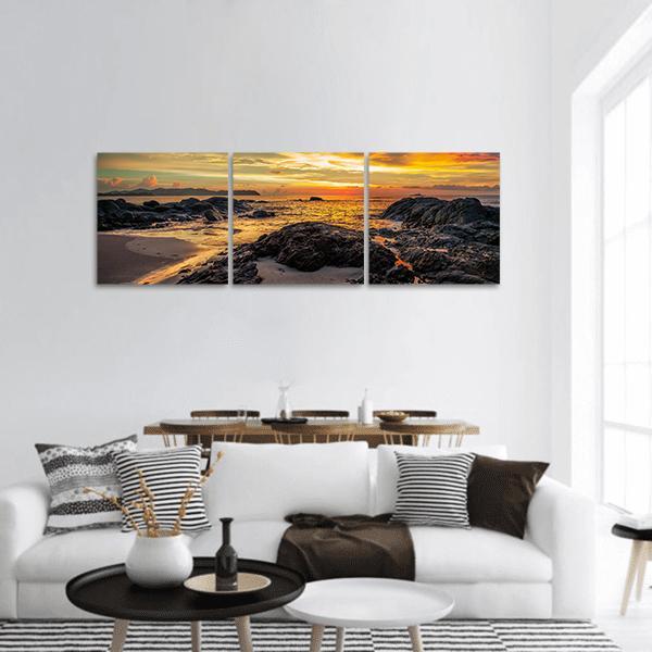 Yellow Sunset Over Rocky Coastline Panoramic Canvas Wall Art in black, orange and yellow, hung on a wall