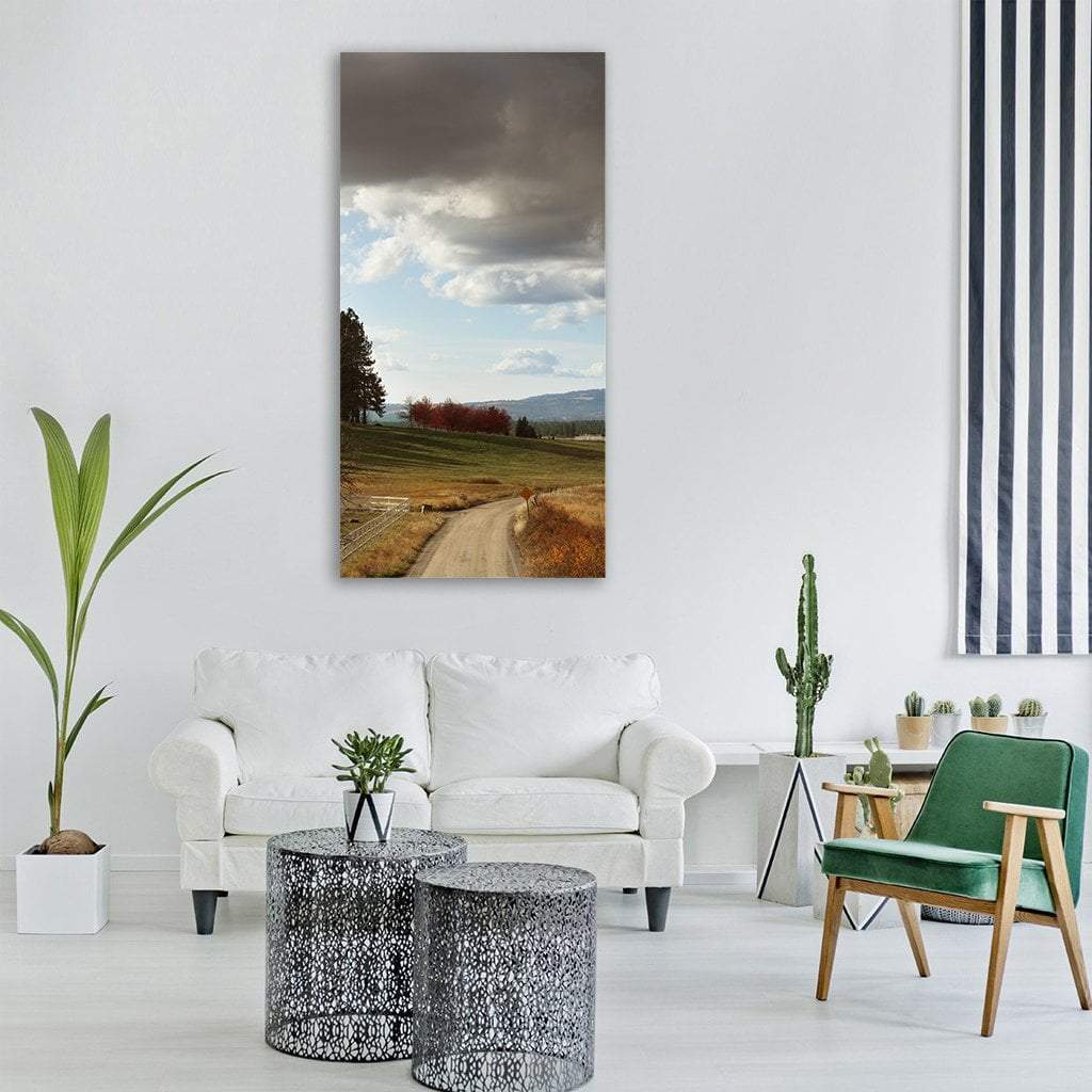 Country Road Under Storm Clouds Vertical Canvas Wall Art in gray, brown and blue, single vertical panel hung on a wall