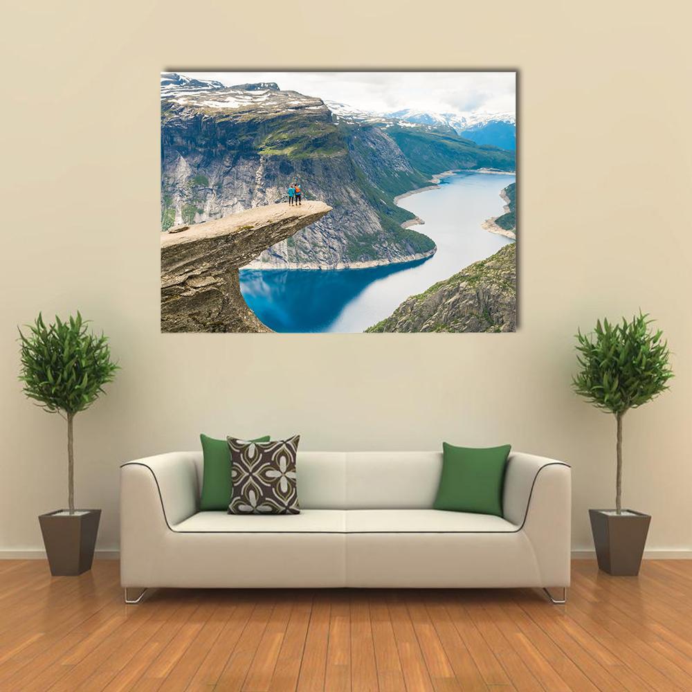 Couple on Trolltunga Cliff Overlooking Lake Canvas Wall Art in gray, green and blue, single panel hung on a wall