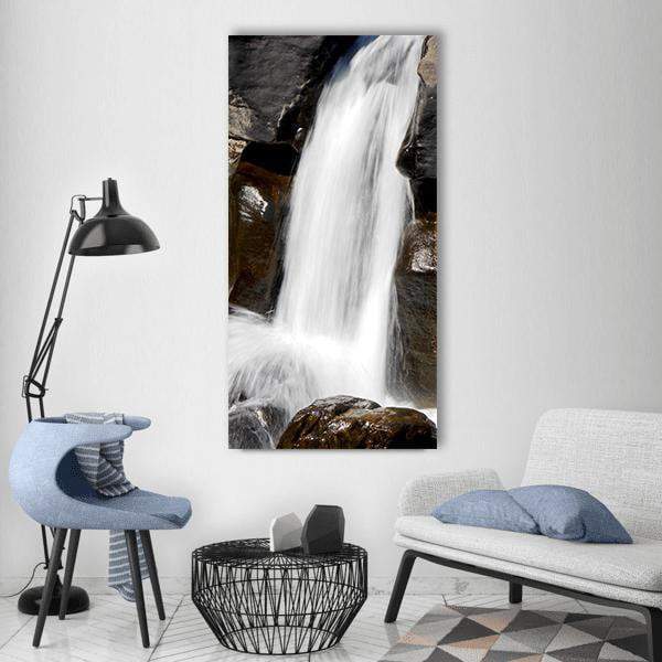 White Waterfall Over Rocks Vertical Canvas Wall Art in black, white and brown, single vertical panel hung on a wall