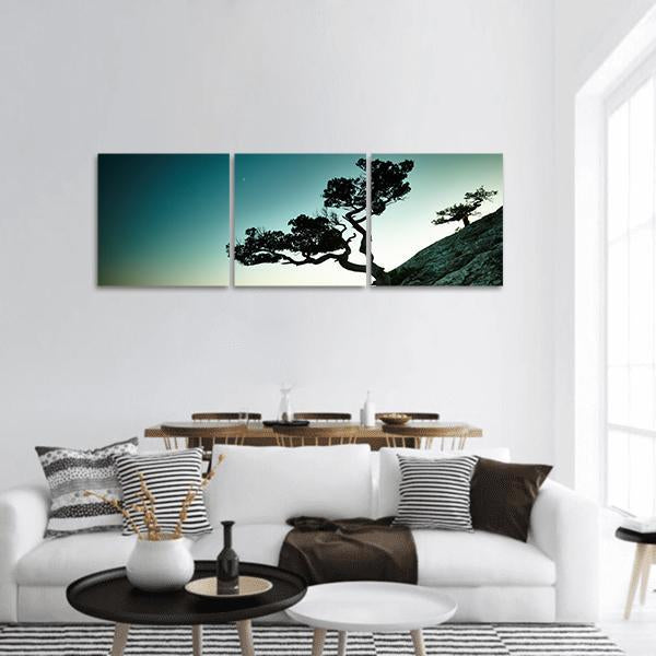 Gnarled Tree at Sunset Over the Sea Panoramic Canvas Wall Art in black, green and blue, hung on a wall