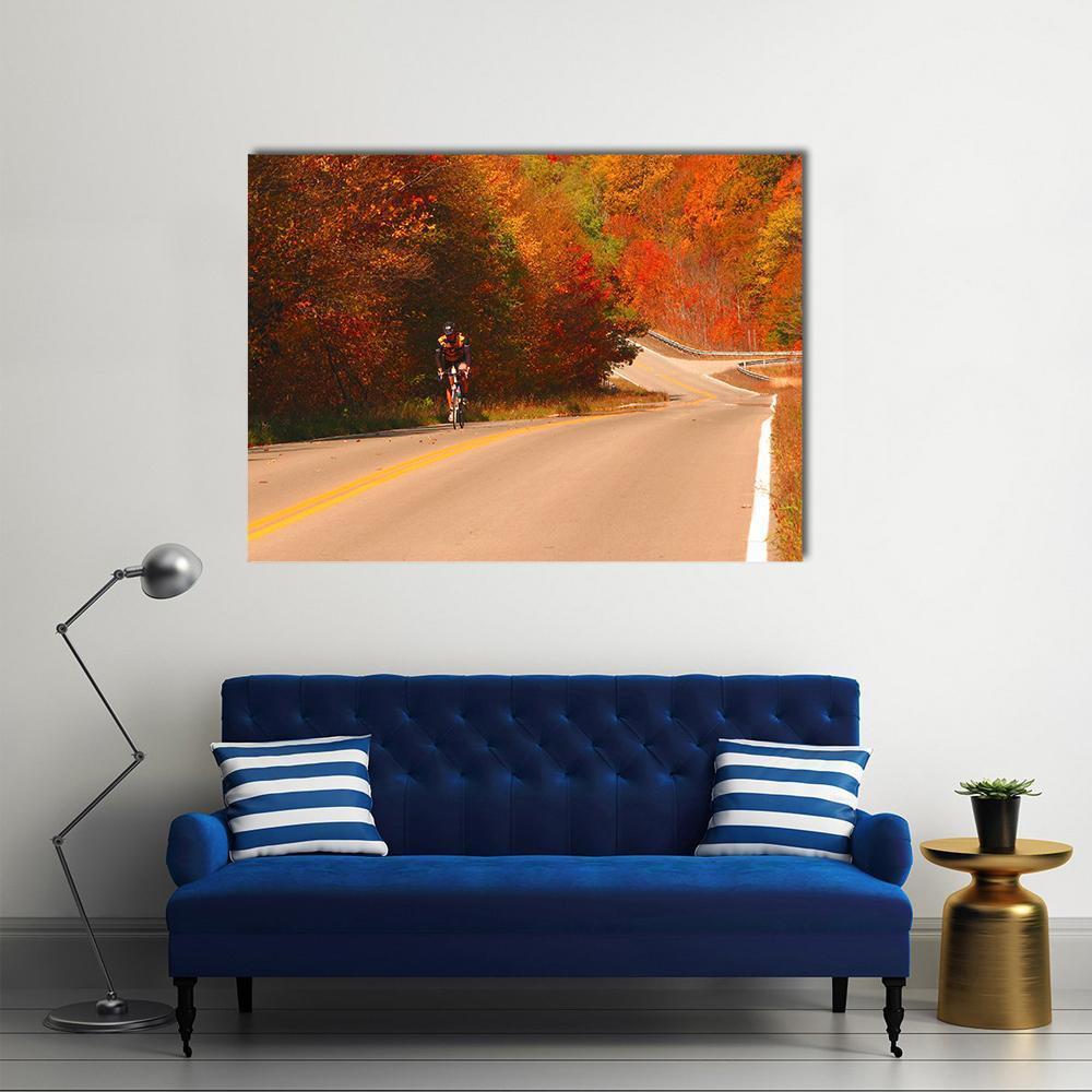 Cyclist on Winding Autumn Road Canvas Wall Art in red, orange and yellow, single panel hung on a wall