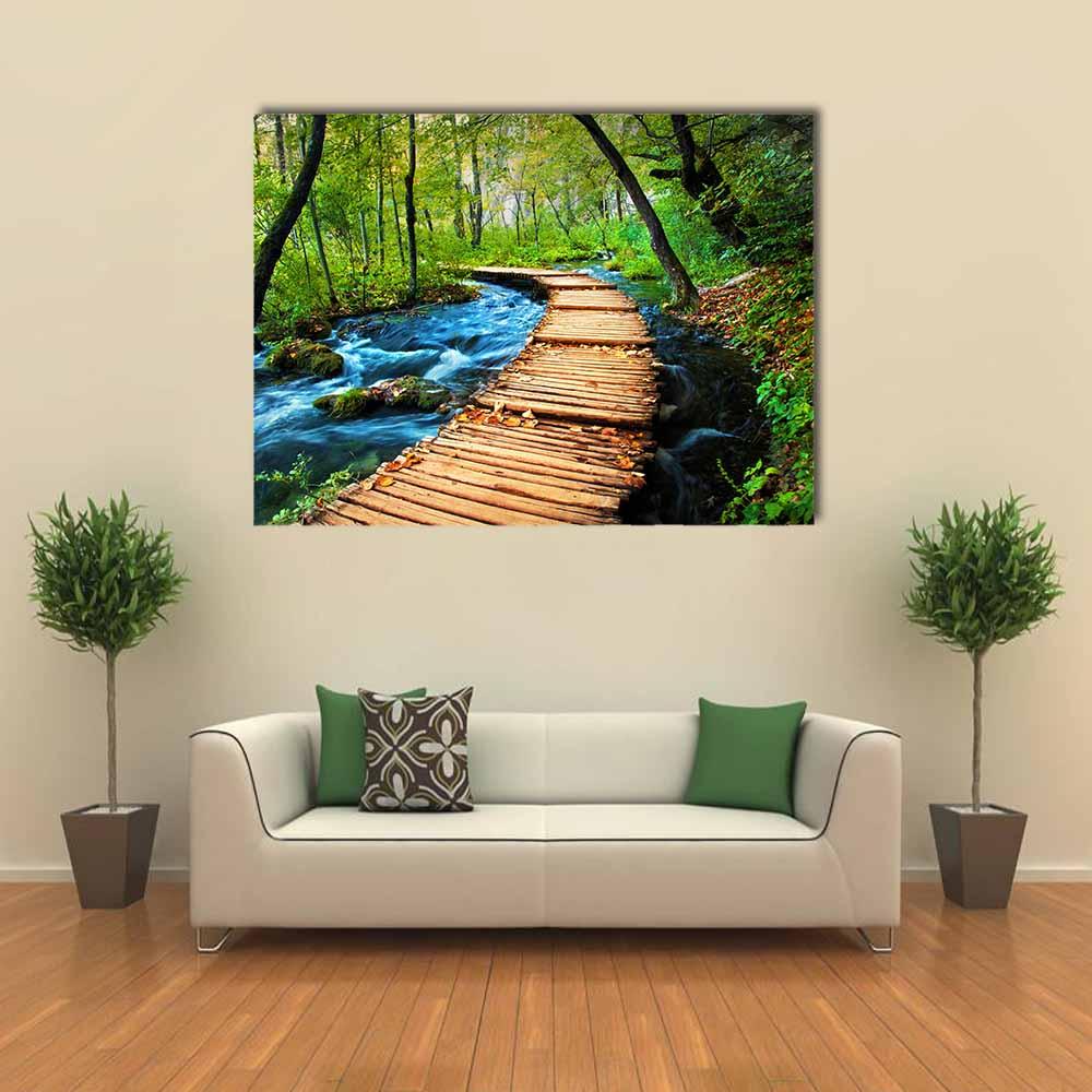 Wooden Boardwalk by Forest Stream Canvas Wall Art in brown, green and blue, single panel hung on a wall