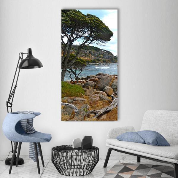 Driftwood on Rocky Beach Vertical Canvas Wall Art in brown, green and blue, single vertical panel hung on a wall