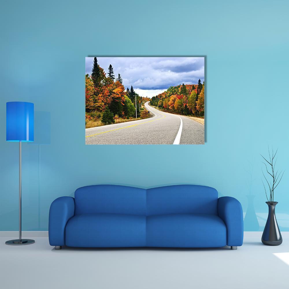 Winding Autumn Highway Through Forest Canvas Wall Art in gray, orange and green, single panel hung on a wall