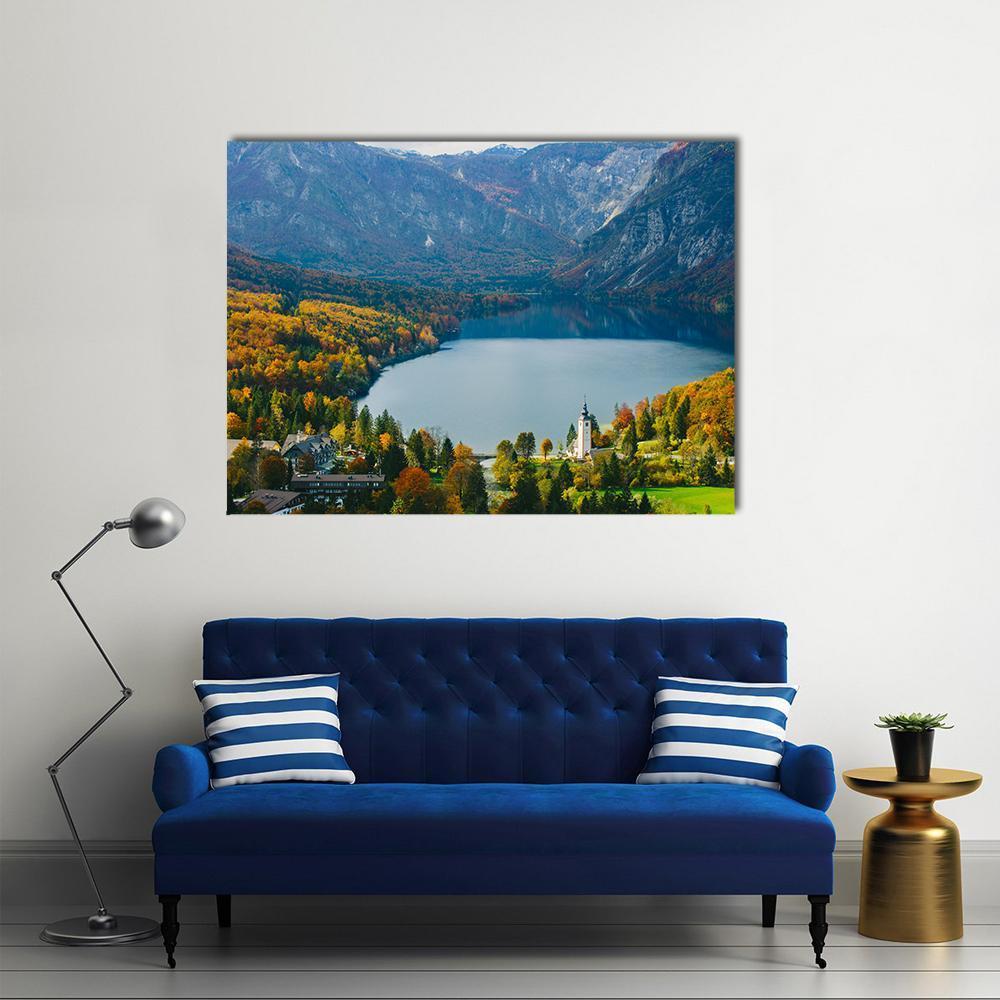 Autumn Lake with Church and Mountains Canvas Wall Art in orange, yellow and blue, single panel hung on a wall
