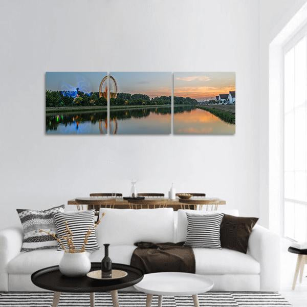 Glowing Ferris Wheel Over River Reflections Panoramic Canvas Wall Art in orange, green and blue, hung on a wall
