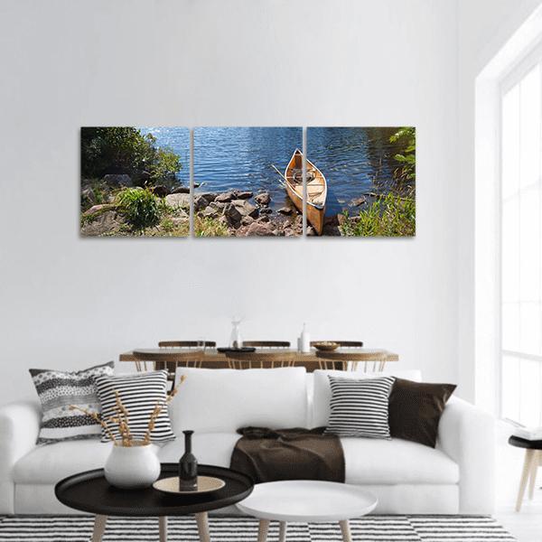 Yellow Canoe on Rocky Shore Panoramic Canvas Wall Art in brown, yellow and blue, hung on a wall