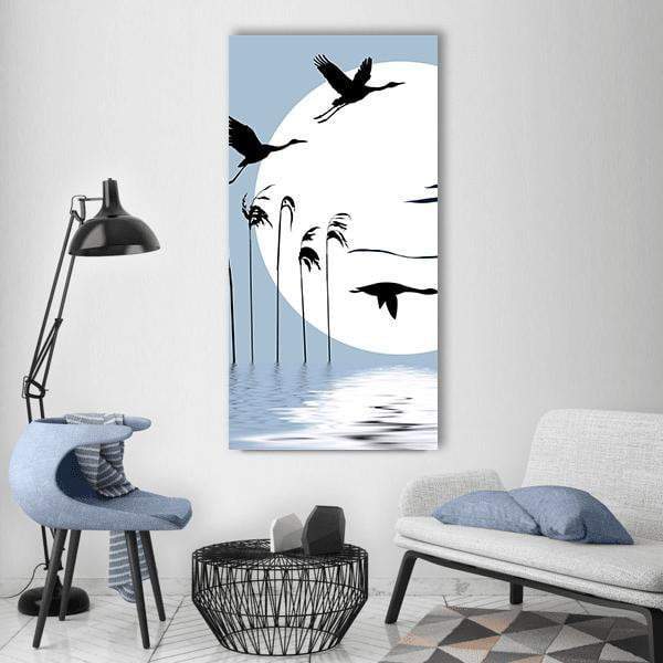 Three Cranes Silhouetted at Moonlit Lake Vertical Canvas Wall Art in black, white and blue, single vertical panel hung on a wall