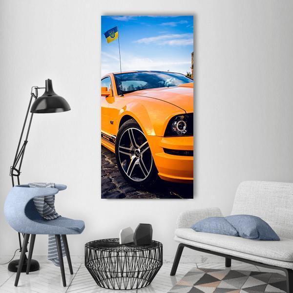 Orange Mustang Gt on Cobblestone Street Vertical Canvas Wall Art in black, orange and blue, single vertical panel hung on a wall