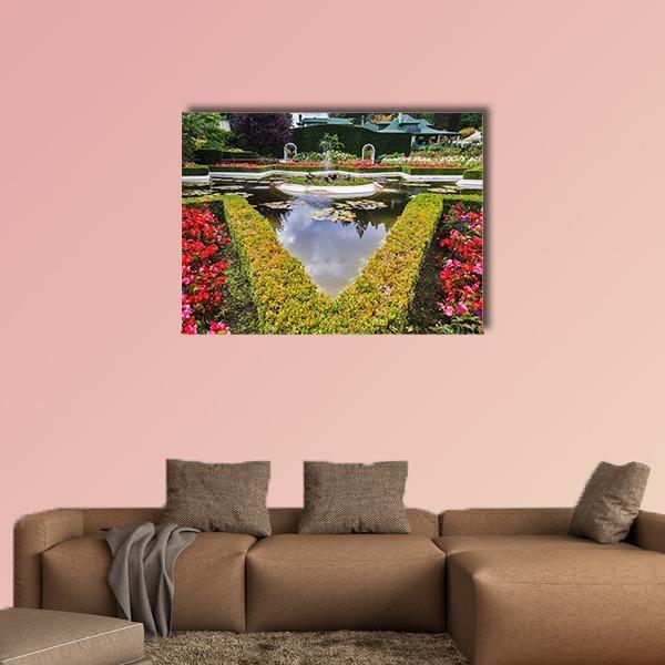 Formal Garden Fountain with Pond Reflection Canvas Wall Art in red and green, single panel hung on a wall