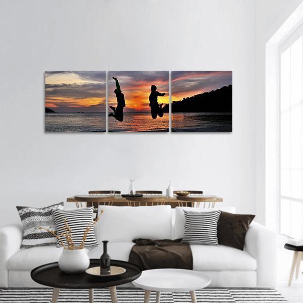 Friends Jumping at Sunset Panoramic Canvas Wall Art in black, orange and yellow, hung on a wall