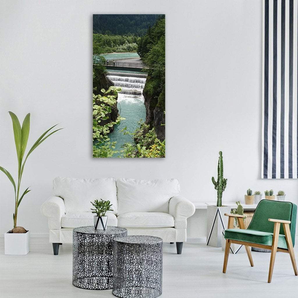 Turquoise River with Footbridge and Waterfall Vertical Canvas Wall Art in green and blue, single vertical panel hung on a wall