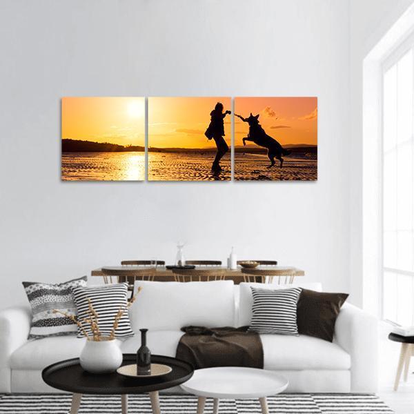Girl Playing with Dog at Sunset Beach Panoramic Canvas Wall Art in black, orange and yellow, hung on a wall