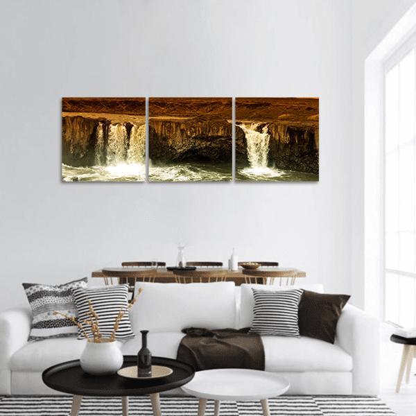 Godafoss Waterfalls Over Rocky Ledge Panoramic Canvas Wall Art in black, brown and yellow, hung on a wall