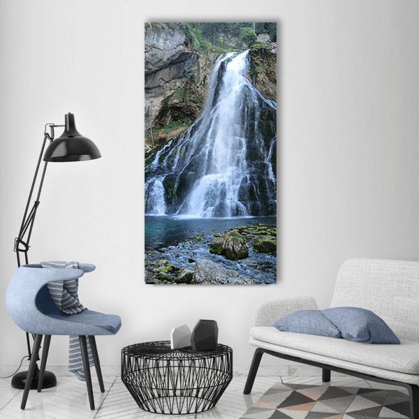 Golling Waterfall Over Mossy Rocks Vertical Canvas Wall Art in white, gray and blue, single vertical panel hung on a wall