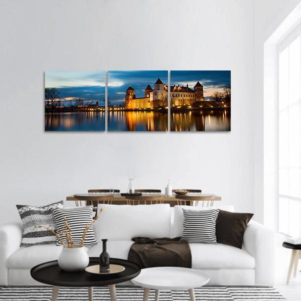 Illuminated Castle Reflection at Dusk Panoramic Canvas Wall Art in orange, yellow and blue, hung on a wall