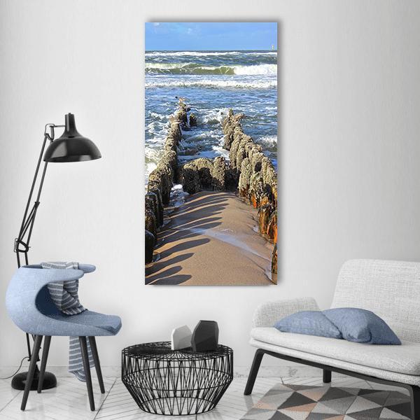 Wooden Breakwater on Sandy Beach Vertical Canvas Wall Art in beige, brown and blue, single vertical panel hung on a wall