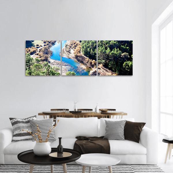 Winding Blue River Through Evergreen Canyon Panoramic Canvas Wall Art in brown, green and blue, hung on a wall