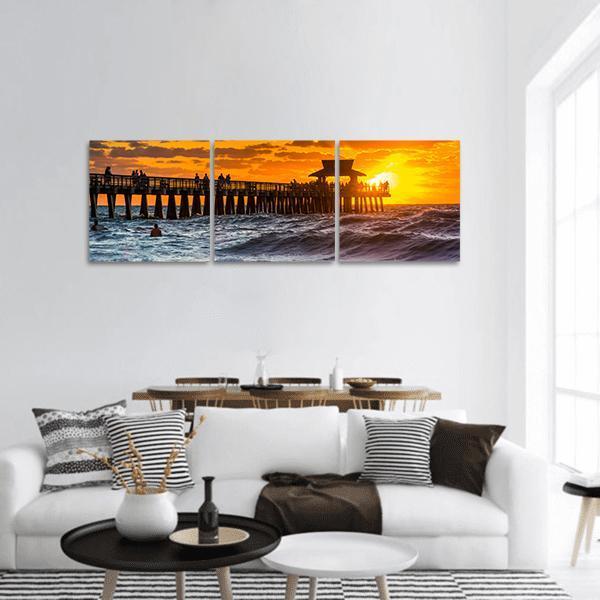 Sunset Over Fishing Pier Panoramic Canvas Wall Art in orange, yellow and blue, hung on a wall