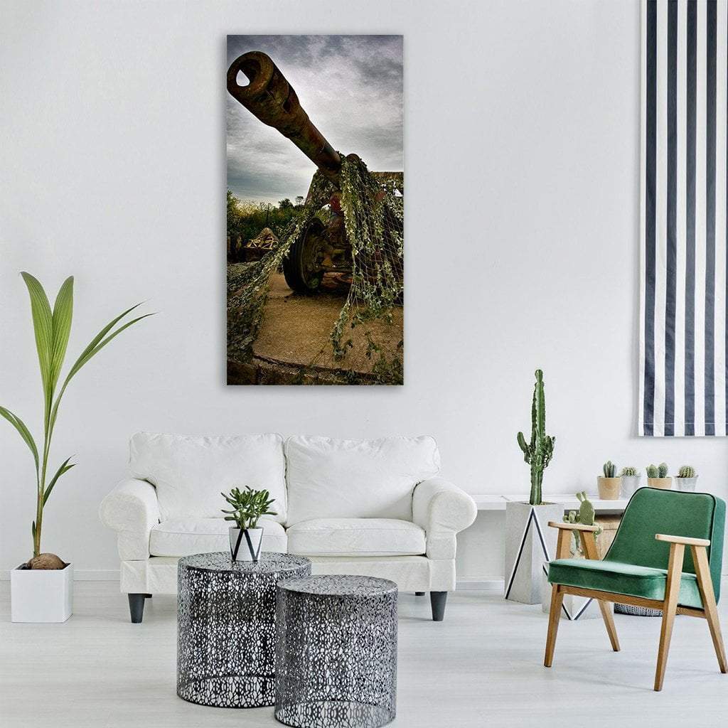 Weathered Artillery Cannon Under Overcast Sky Vertical Canvas Wall Art in gray, brown and green, single vertical panel hung on a wall