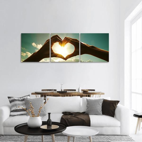 Hands Forming Heart with Sunlight Panoramic Canvas Wall Art in brown, yellow and blue, hung on a wall