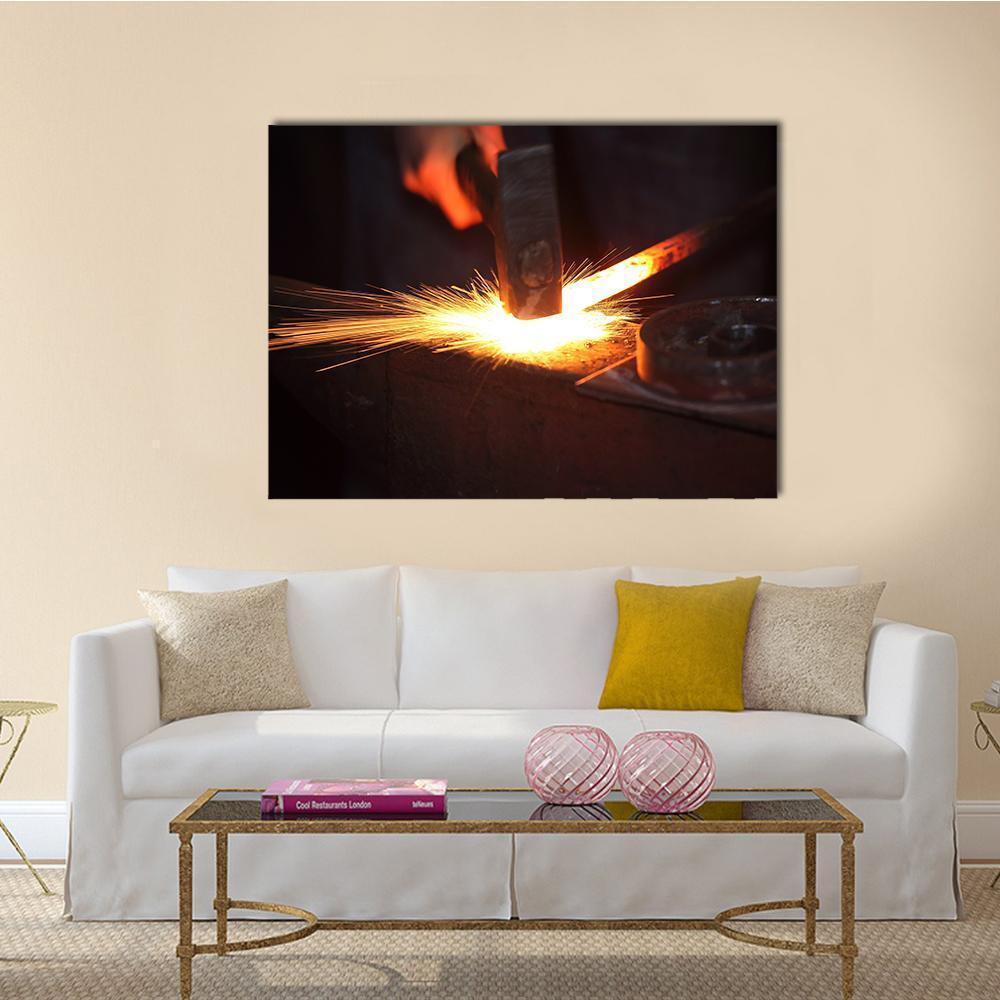 Blacksmith Hands Striking Glowing Metal Canvas Wall Art in black, orange and yellow, single panel hung on a wall