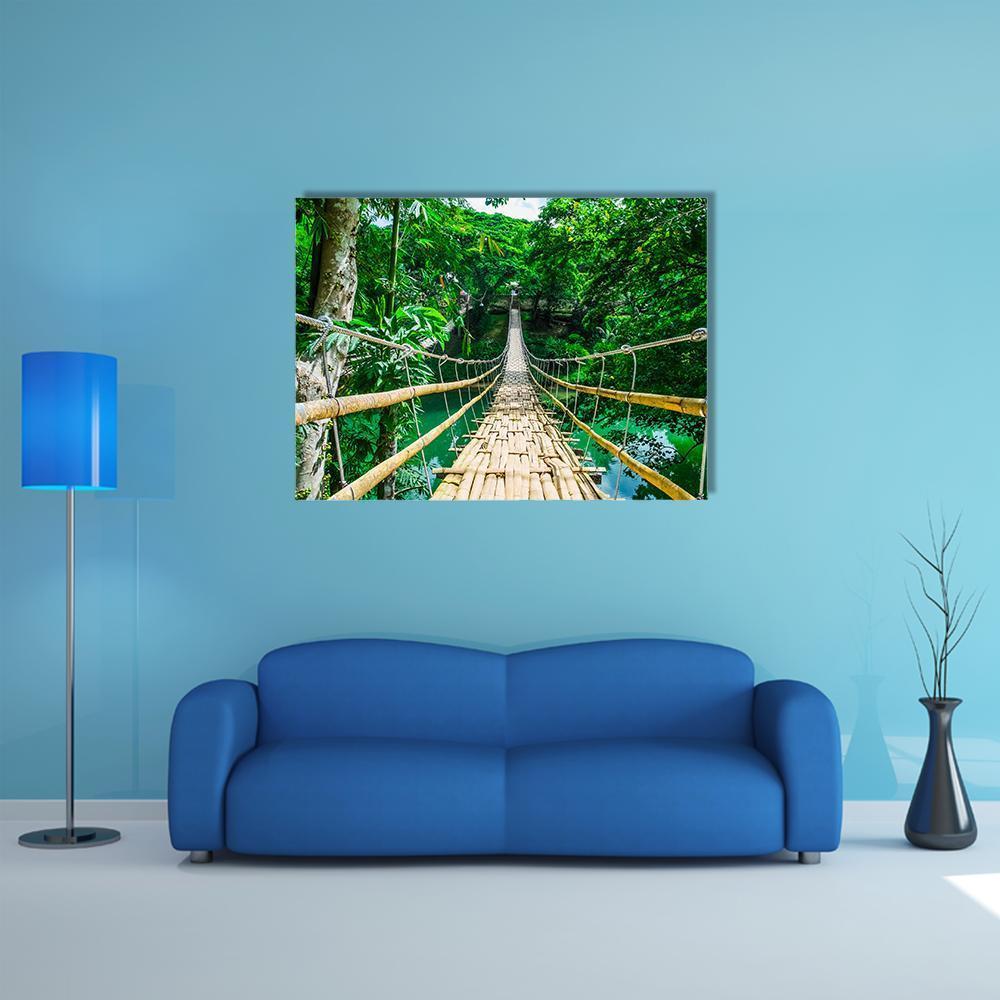 Bamboo Suspension Bridge Over Blue-green River Canvas Wall Art in brown, green and blue, single panel hung on a wall