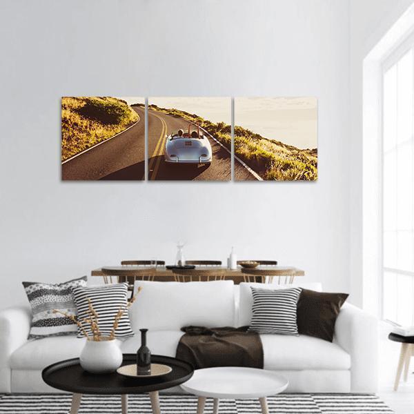 Couple Driving Vintage Convertible on Coastal Road Panoramic Canvas Wall Art in gray, beige and yellow, hung on a wall