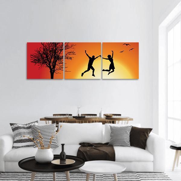 Silhouetted Couple Jumping at Sunset Panoramic Canvas Wall Art in black, orange and yellow, hung on a wall