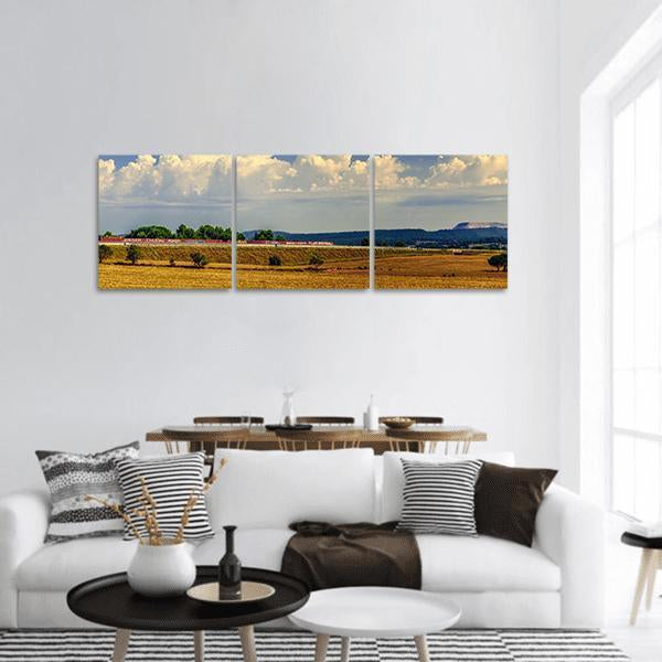 Freight Train Across Golden Field Panoramic Canvas Wall Art in gold, yellow and blue, hung on a wall