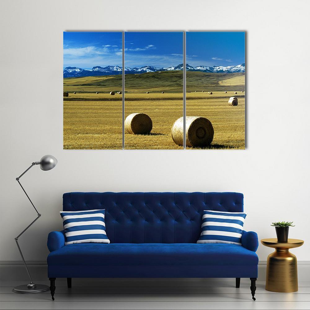 Round Hay Bales with Snow-capped Mountains Canvas Wall Art in brown, yellow and blue, 3 panel horizontal set hung on a wall