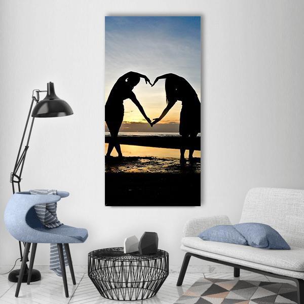 Two Figures Forming Heart on Beach at Sunset Vertical Canvas Wall Art in black, orange and blue, single vertical panel hung on a wall