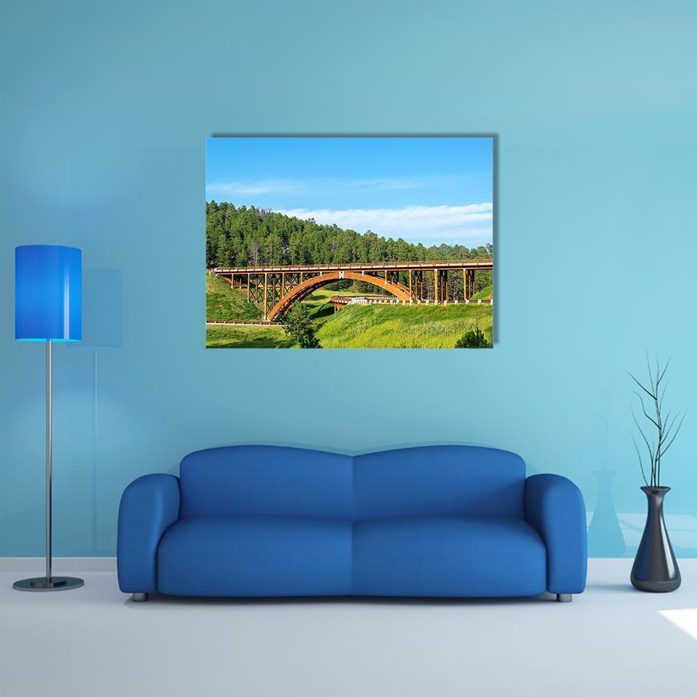 Timber Arch Bridge Over Green Valley Canvas Wall Art in brown, green and blue, single panel hung on a wall