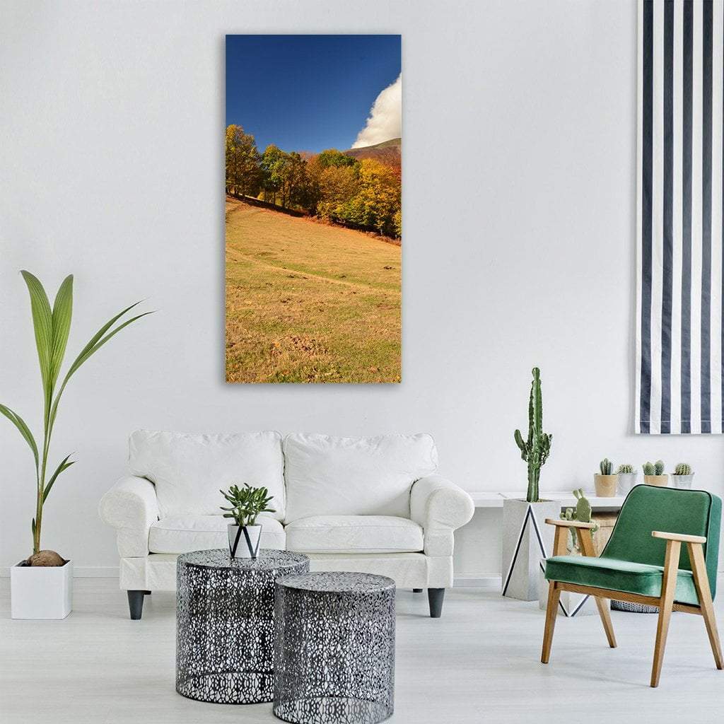 Grassy Hillside with Autumn Trees Vertical Canvas Wall Art in yellow, green and blue, single vertical panel hung on a wall