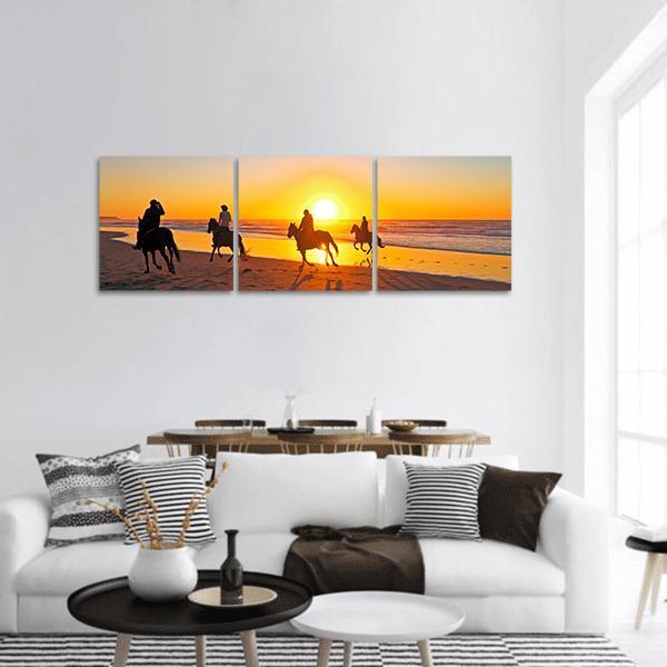 Sunset Horseback Ride on Beach Panoramic Canvas Wall Art in black, orange and yellow, hung on a wall