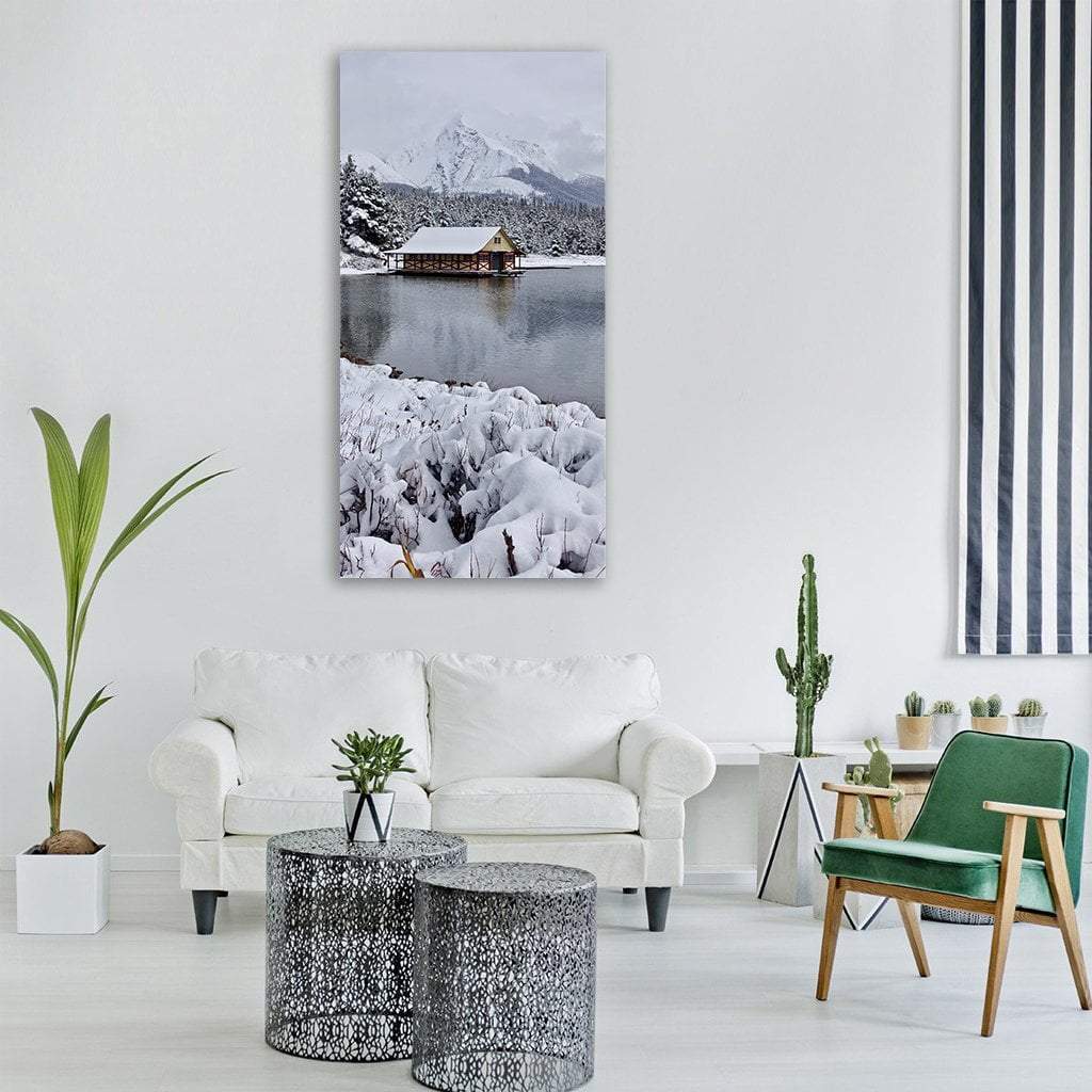 Snowy Cabin by Mountain Lake Vertical Canvas Wall Art in white and gray, single vertical panel hung on a wall