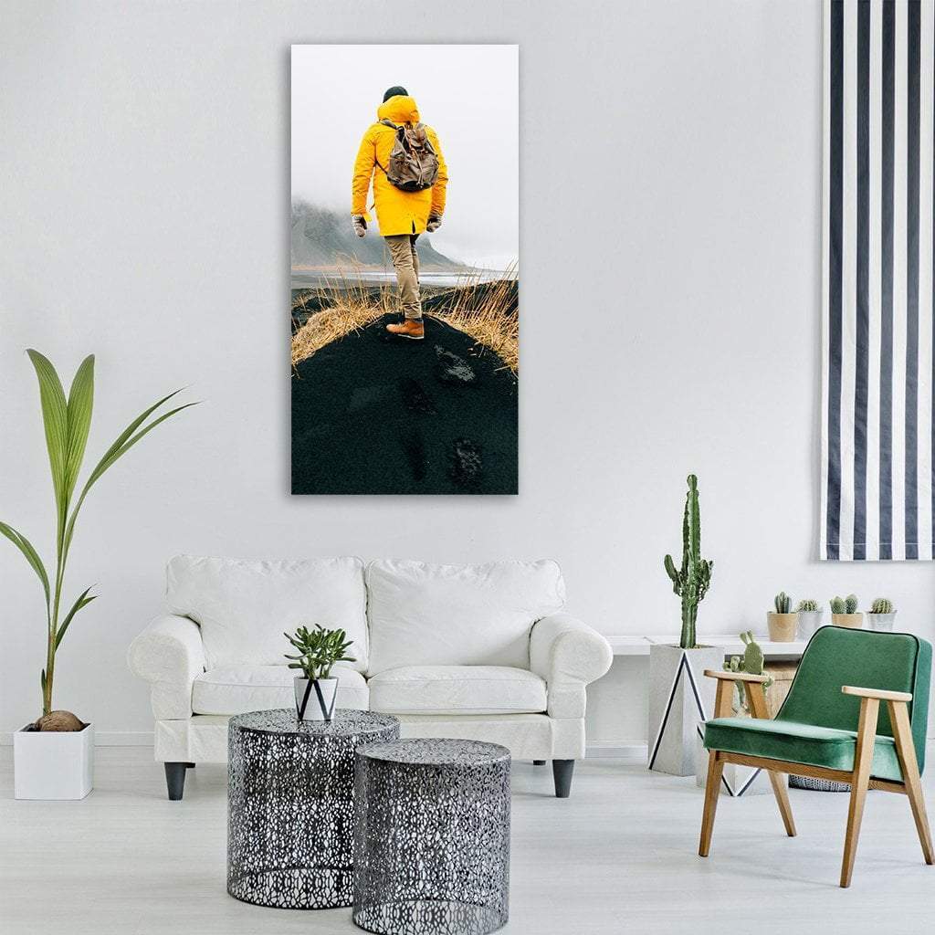 Hiker in Yellow Parka on Volcanic Slope Vertical Canvas Wall Art in black, white and yellow, single vertical panel hung on a wall