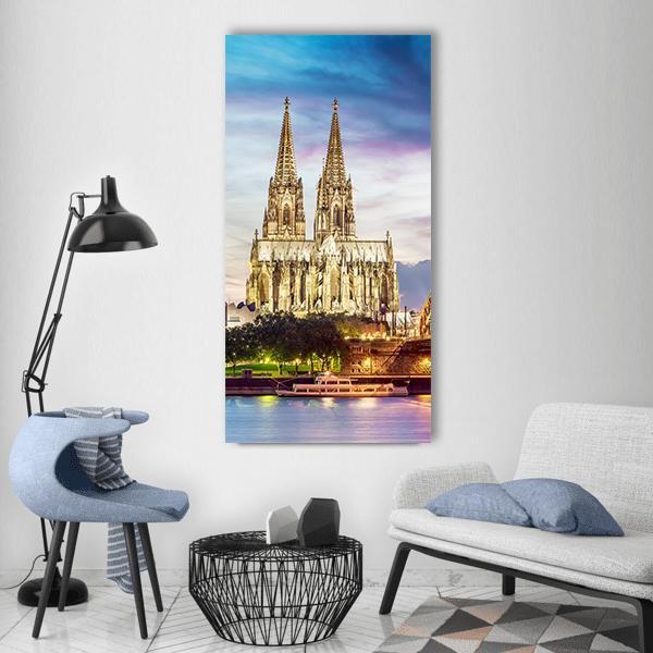 Illuminated Cologne Cathedral at Twilight Vertical Canvas Wall Art in yellow, blue and purple, single vertical panel hung on a wall