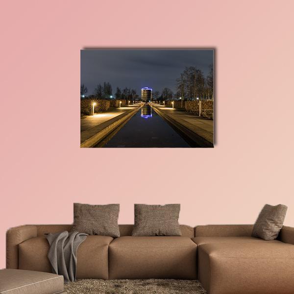 Blue-lit Gasometer with Reflecting Water Canvas Wall Art in black, brown and blue, single panel hung on a wall