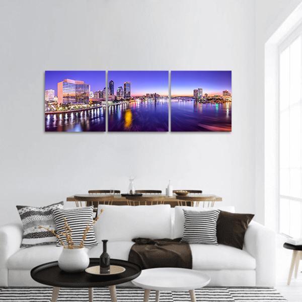 Riverfront City Skyline at Dawn Panoramic Canvas Wall Art in orange, blue and purple, hung on a wall