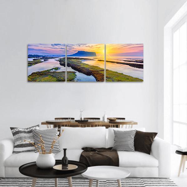 Sunrise Over Mossy Tide Pools Panoramic Canvas Wall Art in orange, yellow and blue, hung on a wall