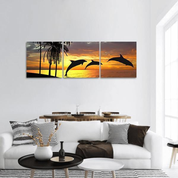 Three Leaping Dolphins at Sunset Panoramic Canvas Wall Art in black, orange and yellow, hung on a wall