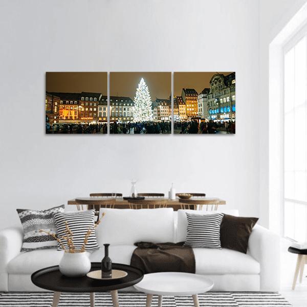 Glowing Christmas Tree in City Square Panoramic Canvas Wall Art in brown, gold and yellow, hung on a wall